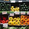 Brightly colored bell peppers and squash sit on a supermarket shelf above prominently displayed price tags.