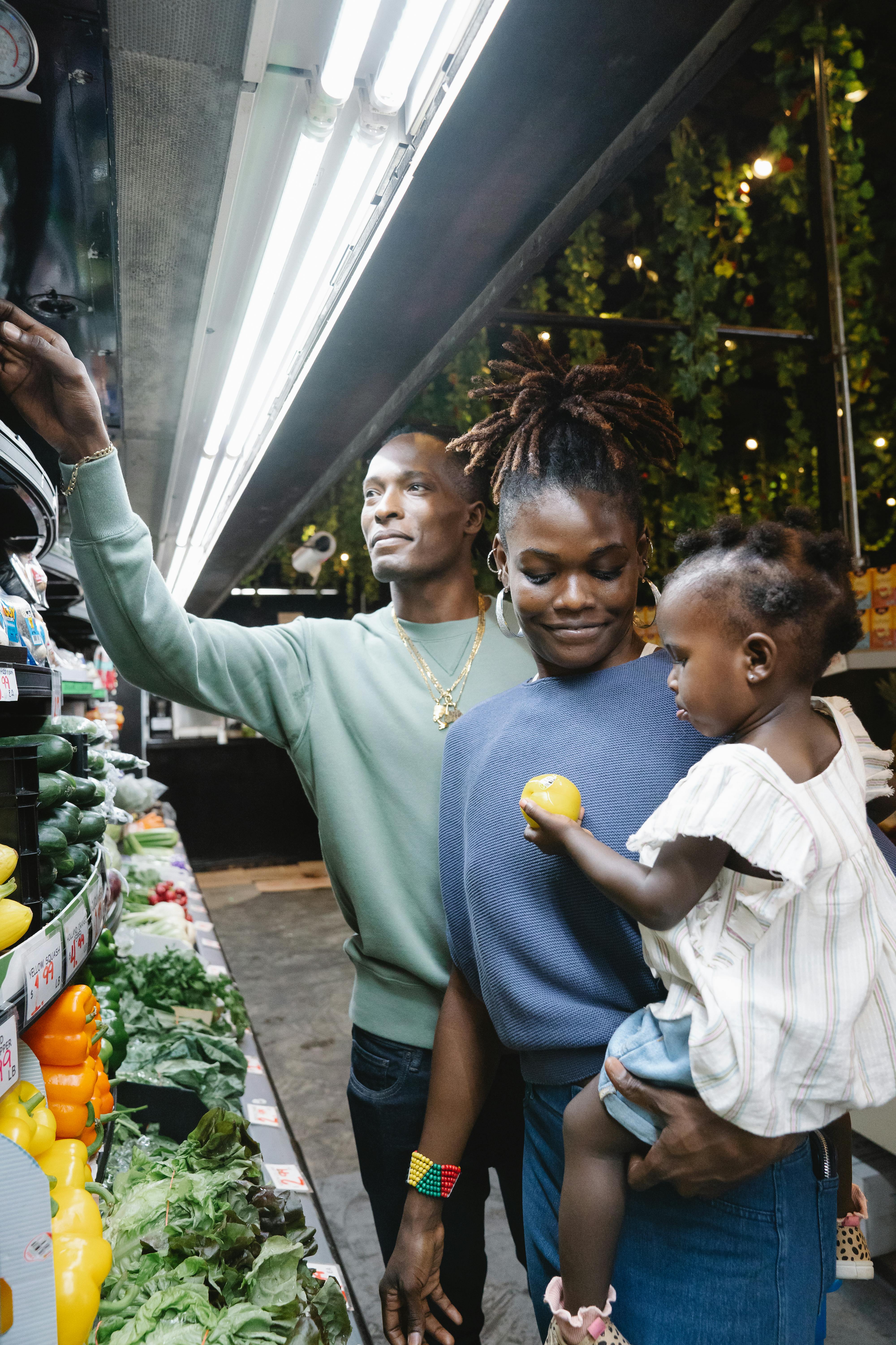 A family with a toddler shopping for fresh produce in a supermarket aisle.