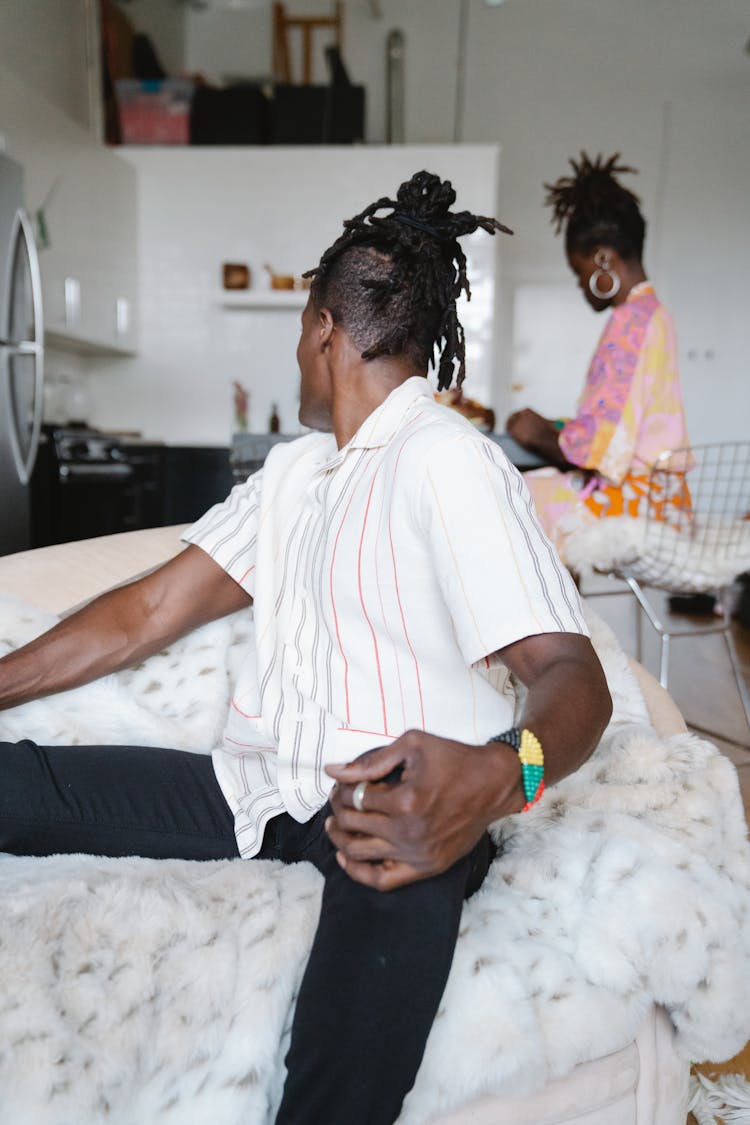 A Man Sitting On A Couch While Looking Back To His Wife