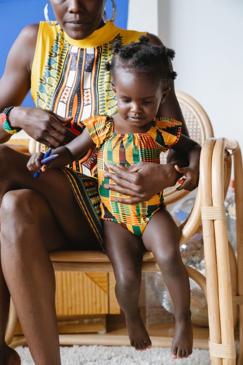 Free Woman and child wearing vibrant African prints sitting on a wooden chair indoors. Stock Photo