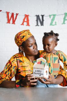Mother and daughter in traditional attire sharing a joyful Kwanzaa celebration with a gift.