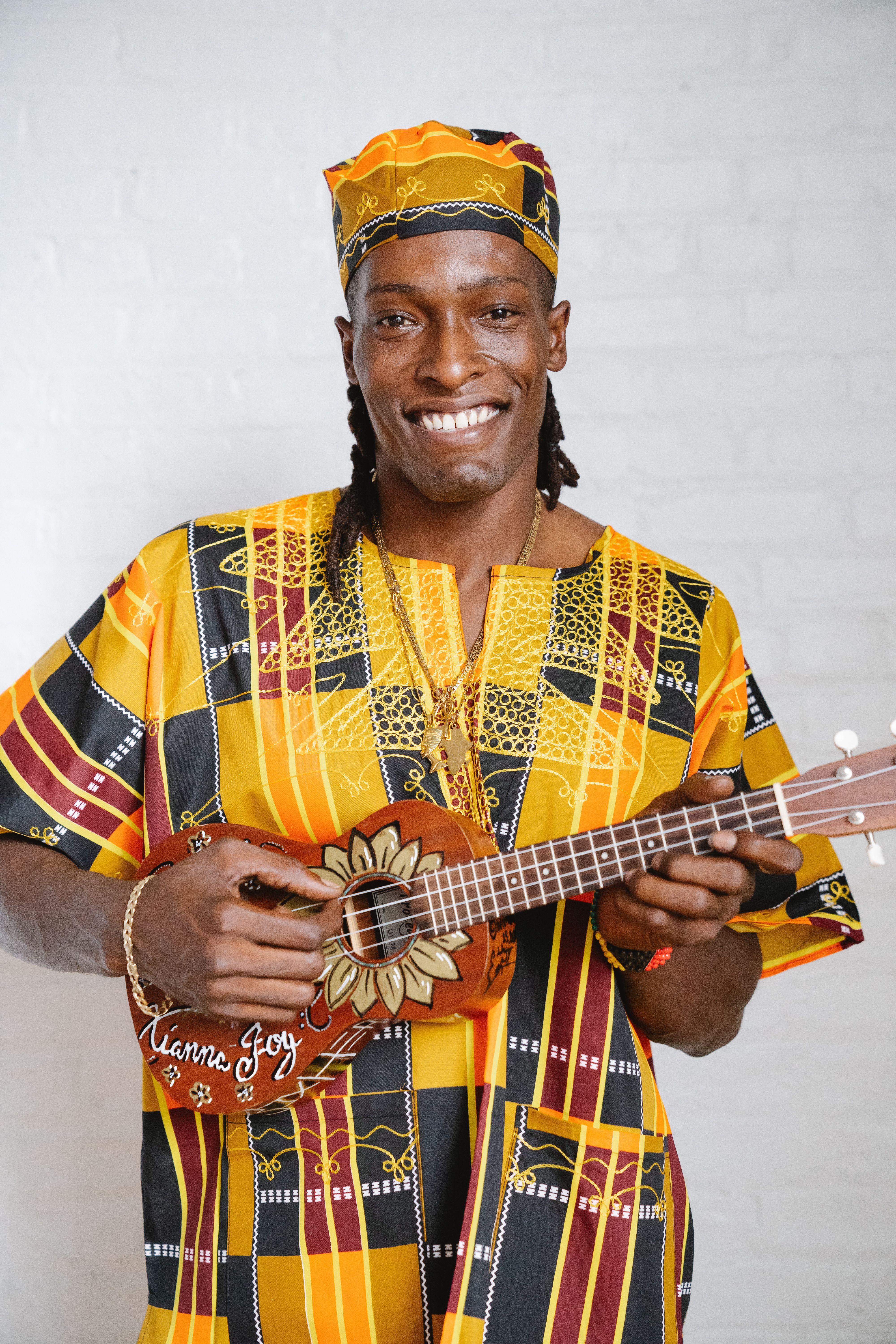 Happy musician in colorful traditional attire playing a handcrafted ukulele.