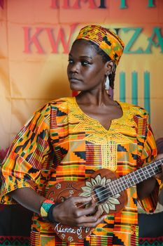 Woman in traditional attire plays ukulele during Kwanzaa celebration.