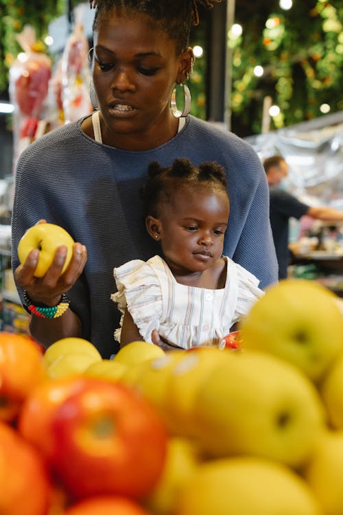 A Mother Buying Fruits while Carrying Her Daughter