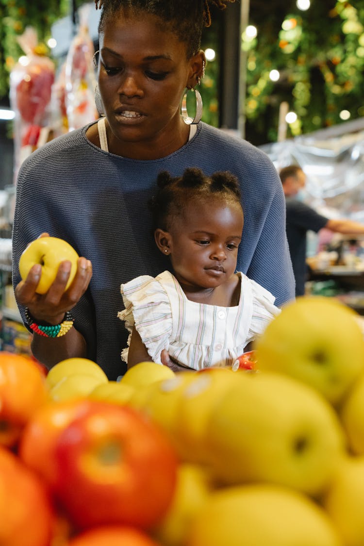 A Mother Buying Fruits While Carrying Her Daughter