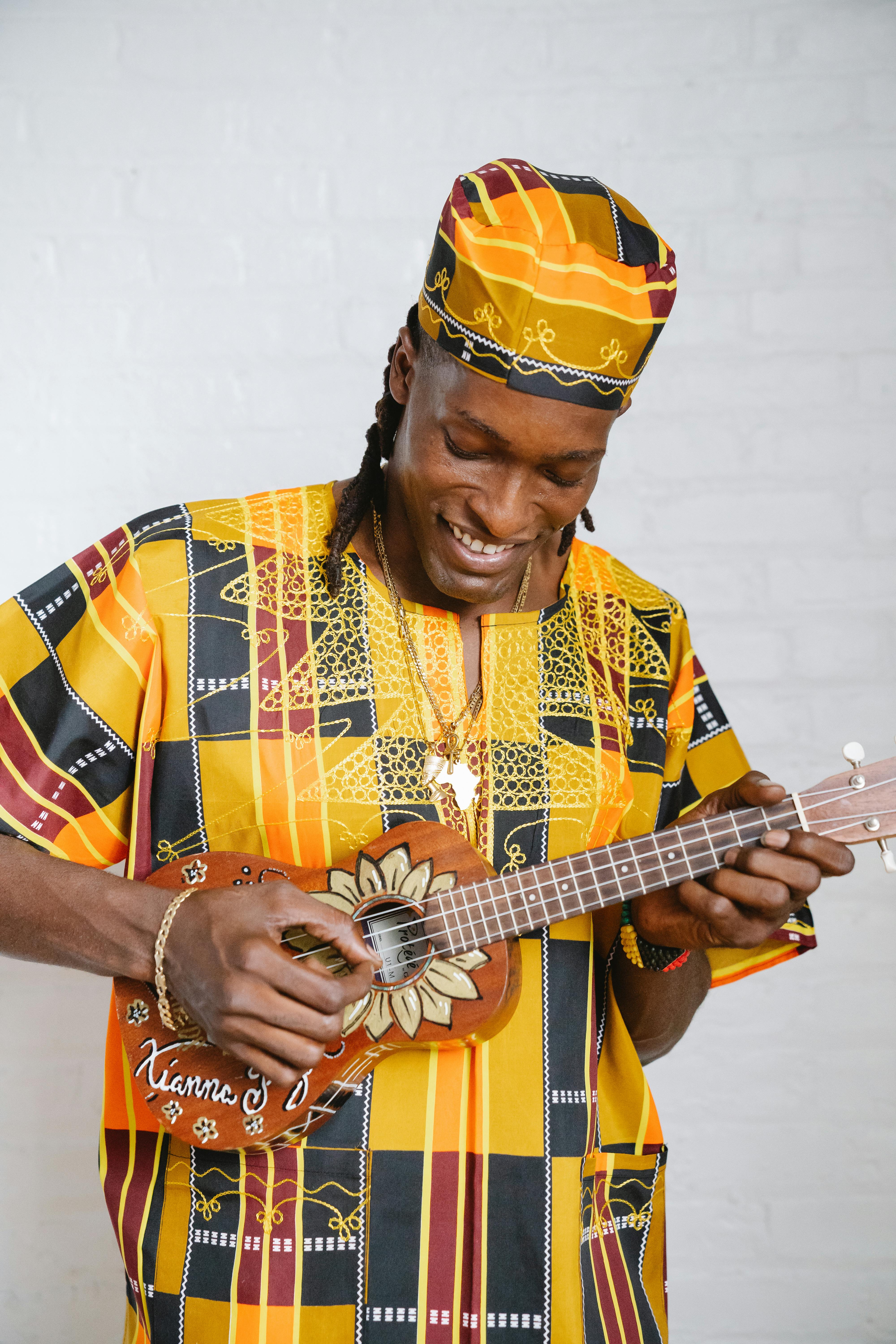 Smiling man in colorful traditional attire playing a ukulele indoors.