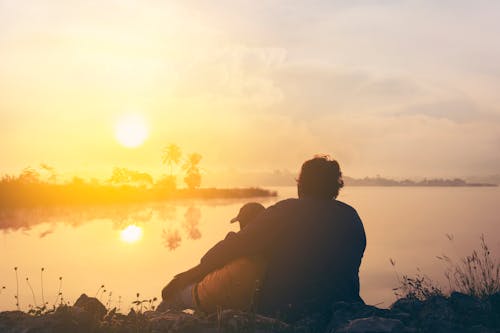 Free Two People On Grass Beside Body Of Water During Golden Hour Stock Photo
