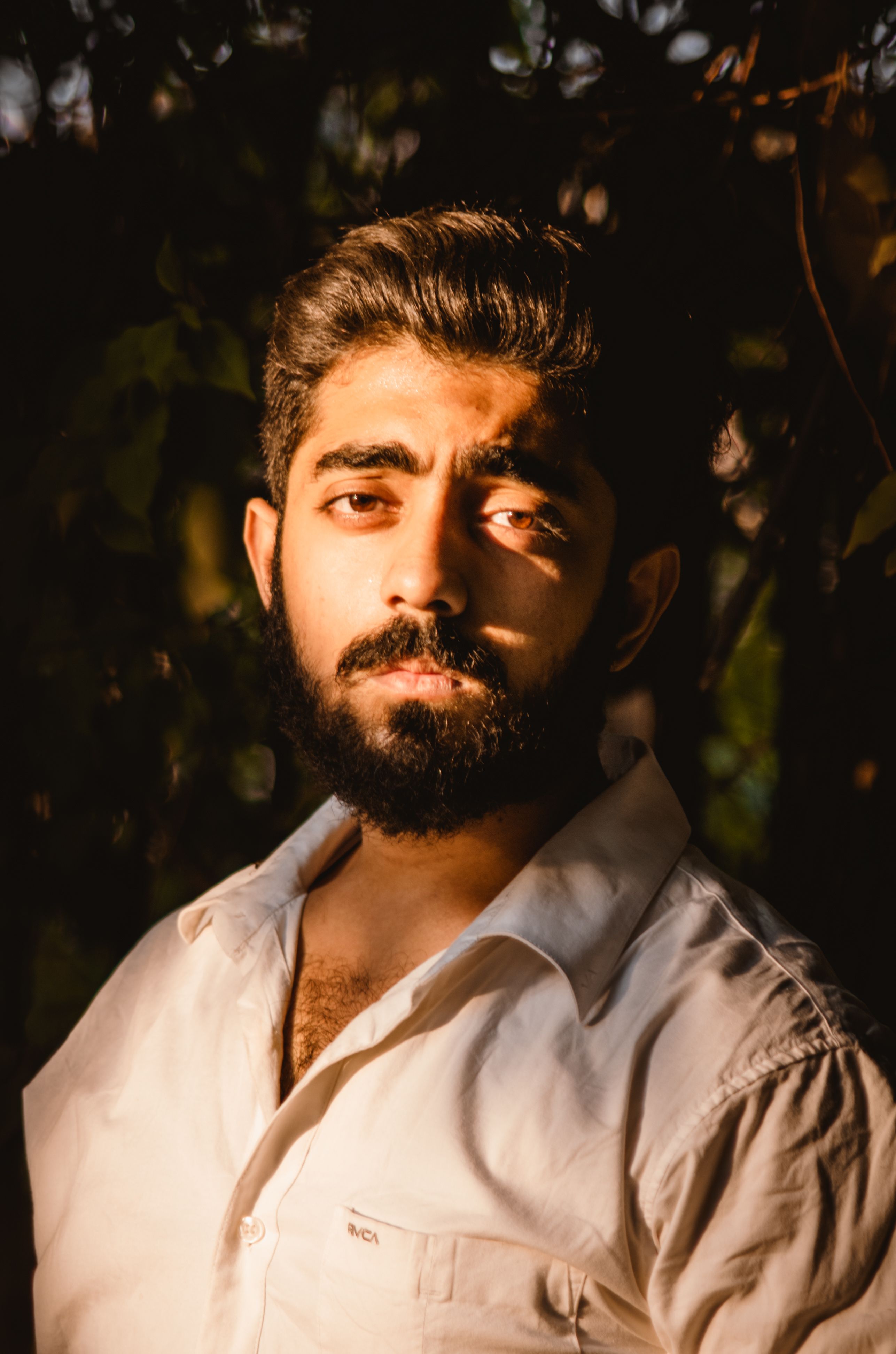 A thoughtful Indian man with a beard in a sunlit portrait, expressing emotion.