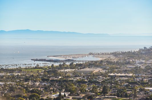 Aerial view of a scenic coastal city with ocean, beach, and mountains under a bright blue sky.