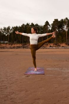 Woman performing a yoga pose on a beach, embodying balance and serenity at sunset.