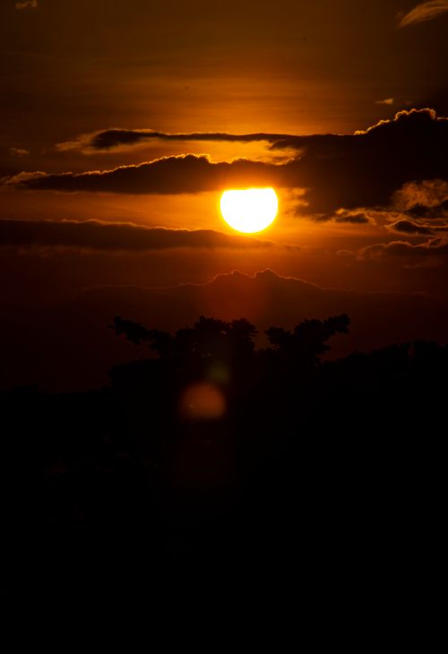 Free A stunning sunset with clouds and silhouetted landscape, creating a dramatic scene. Stock Photo
