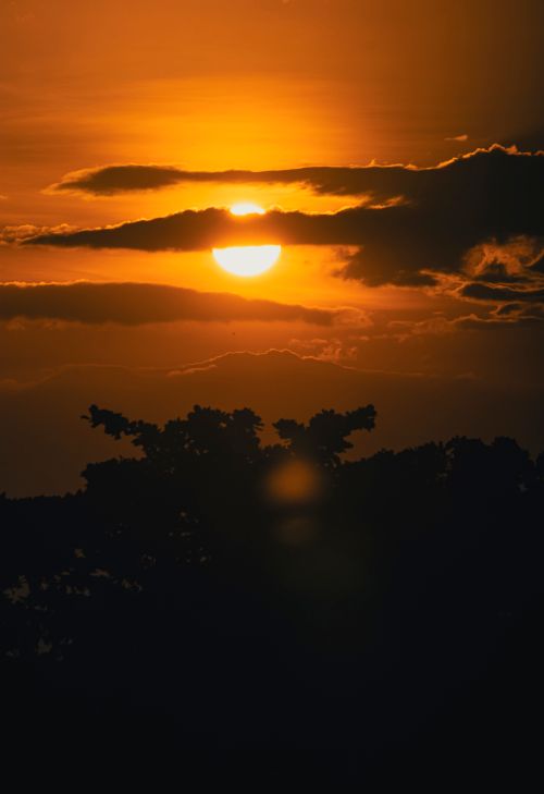 Free A stunning sunset with clouds and tree silhouettes creates a dramatic and warm atmosphere. Stock Photo