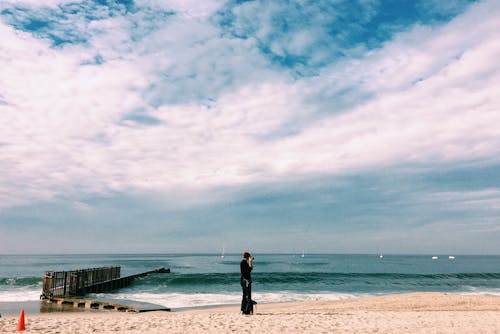 Person in Black Top Standing on Seashore Under White Clouds