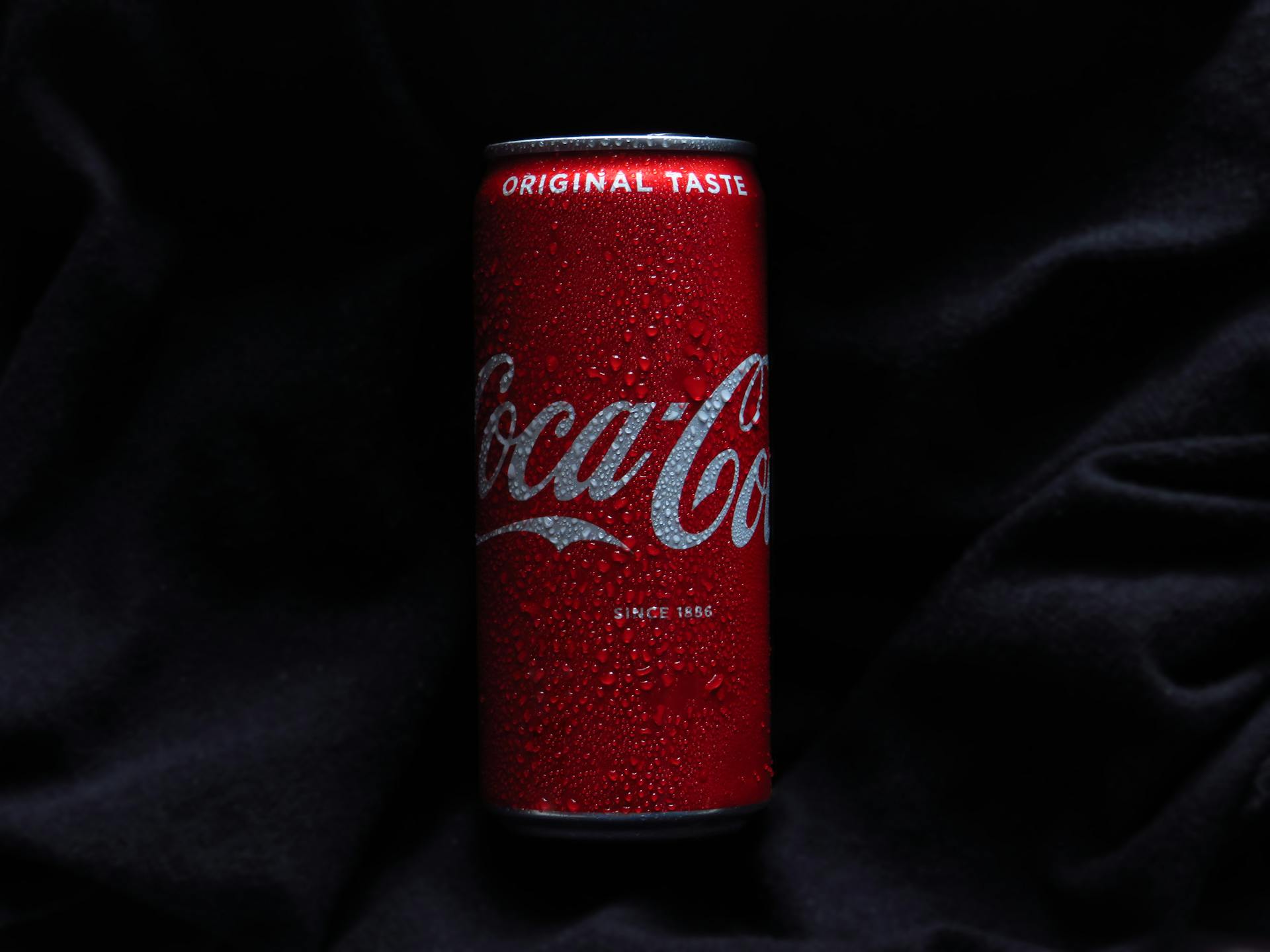 Close-up of a chilled Coca-Cola can covered in water droplets on a black background.