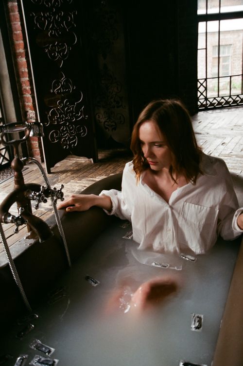 Free A woman in a white shirt enjoying a soothing milk bath indoors. Stock Photo
