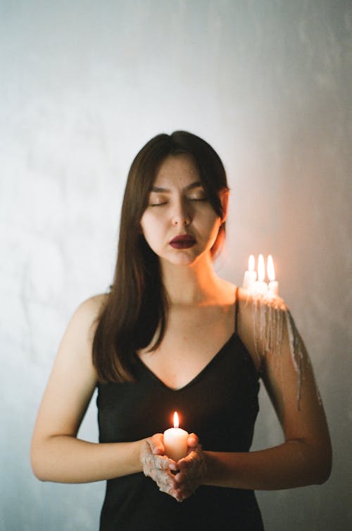 Young woman posing with candle in hands and on shoulder