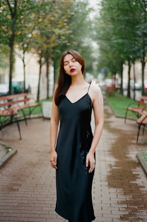 Young woman wearing black dress and posing in park with candle on shoulder