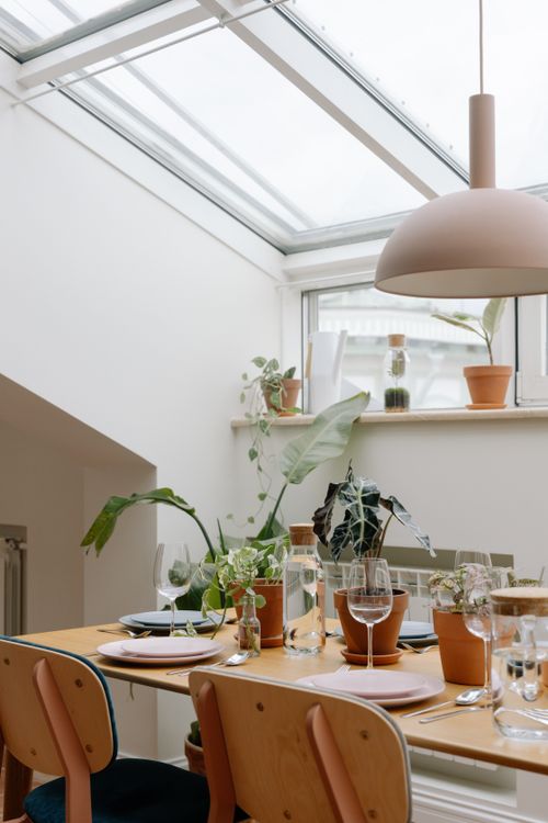 Free A beautifully arranged dining table surrounded by potted plants under a skylight, creating a serene atmosphere. Stock Photo