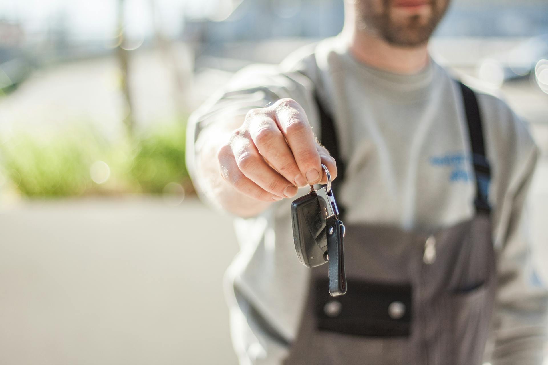 Hand holding a car key outdoors, blurred background, shallow focus.