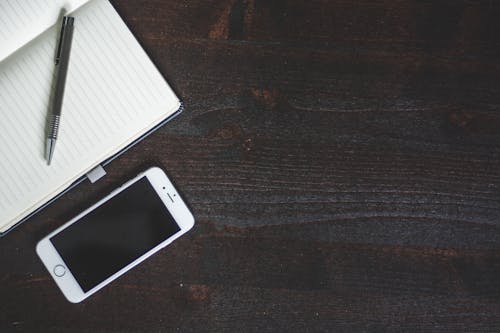 Silver Iphone 6 Beside White Book With Pen