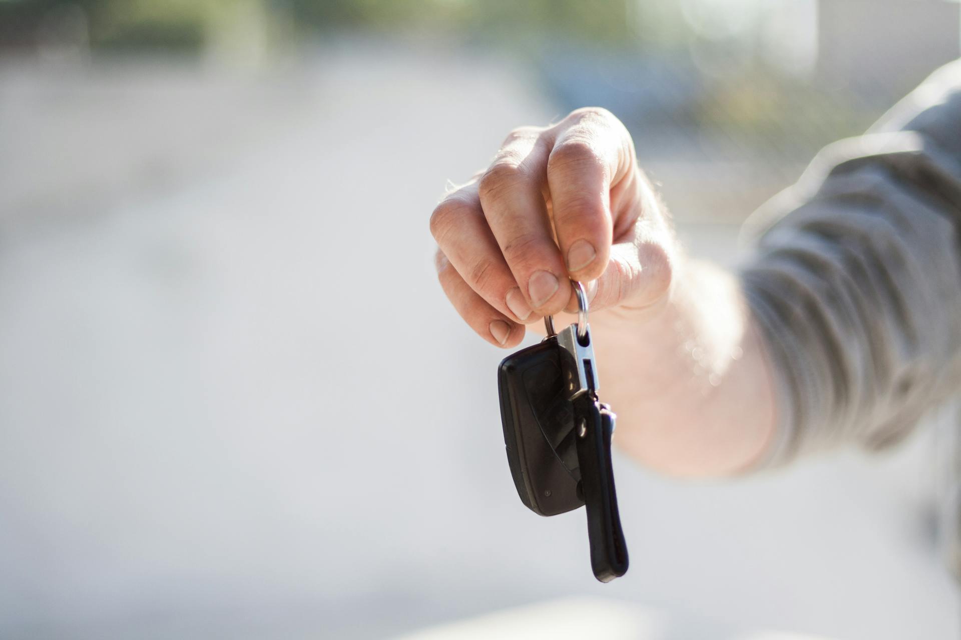 Close-up of a hand handing over car keys, signifying purchase or rental.