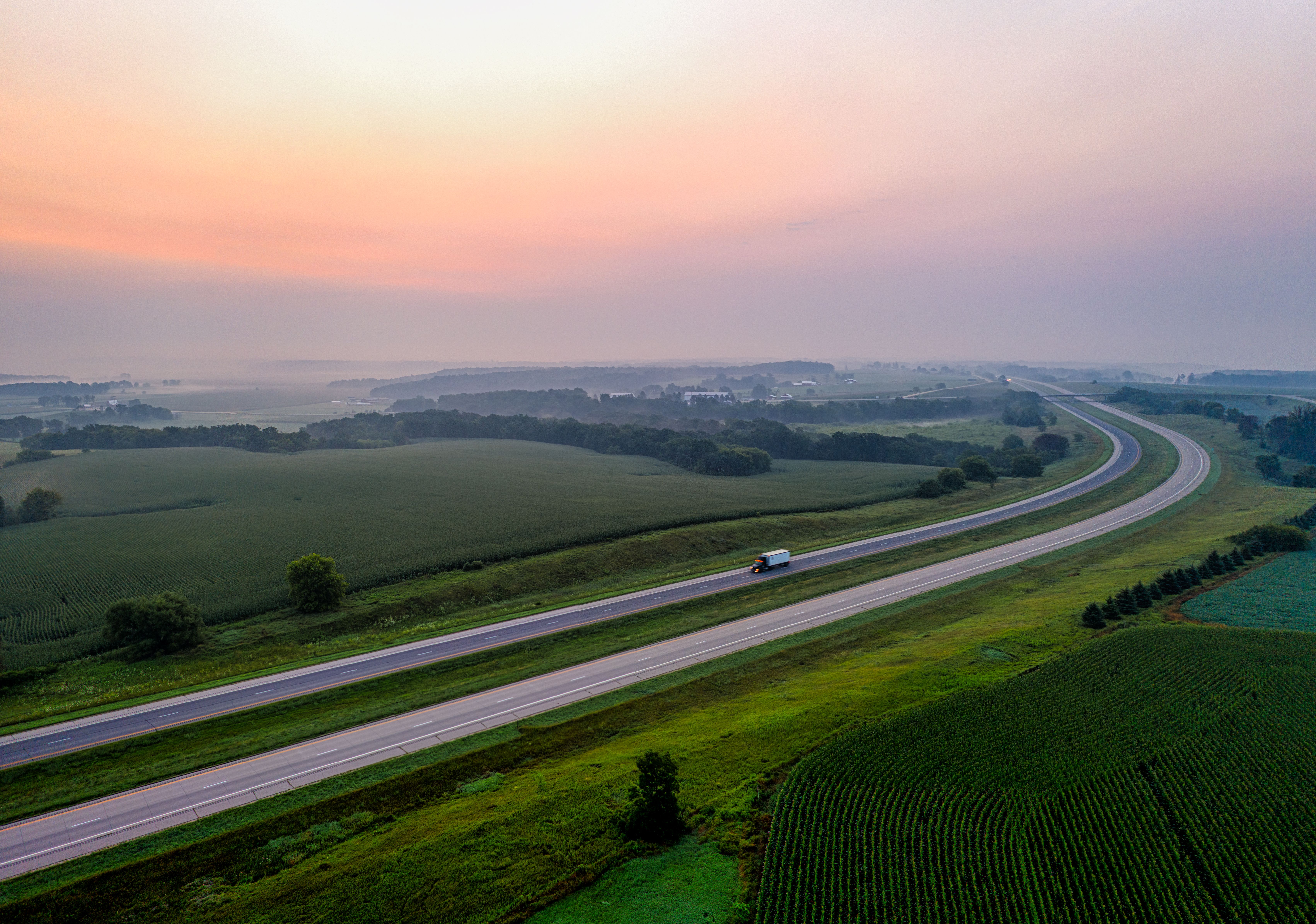 Aerial view of a winding road through lush cropland in Minnesota at sunrise.