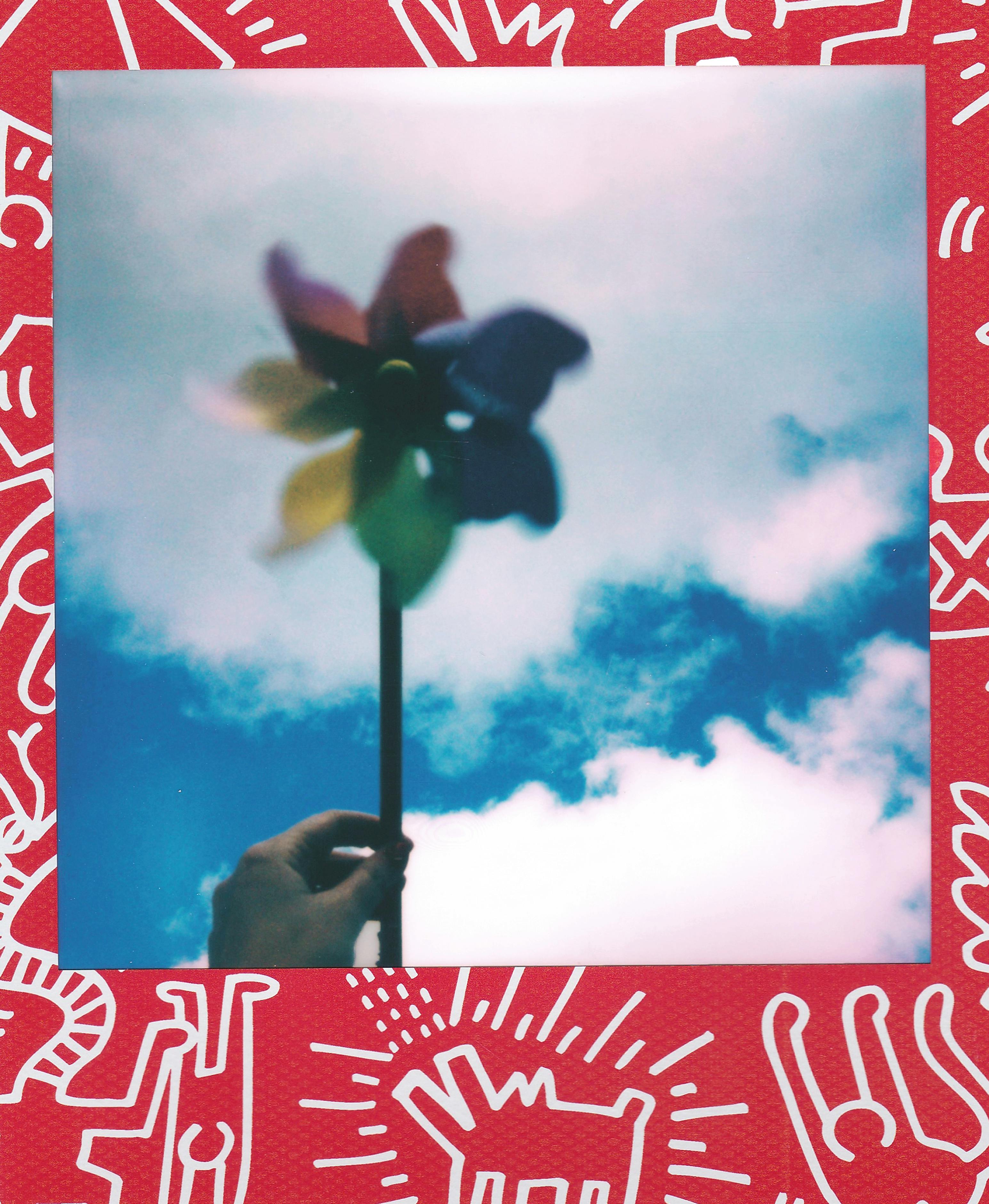 Colorful pinwheel held aloft against a bright cloudy sky with artistic border design.