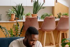 Man reading a book in a modern living area with plants and stylish furniture.
