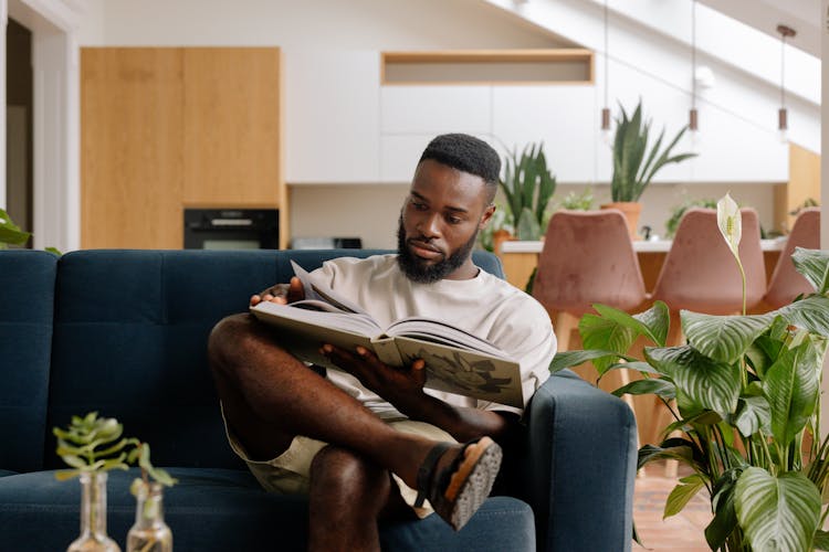 A Man Reading A Book On The Couch 