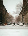 Free A Person Crossing the Snow Covered Street Near Concrete Buildings Stock Photo
