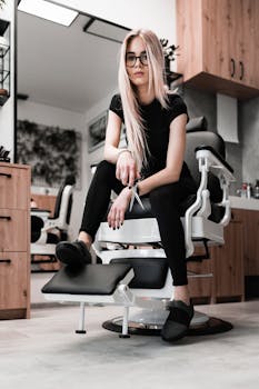 Confident hairstylist in a modern salon holding scissors, seated on a barber chair.