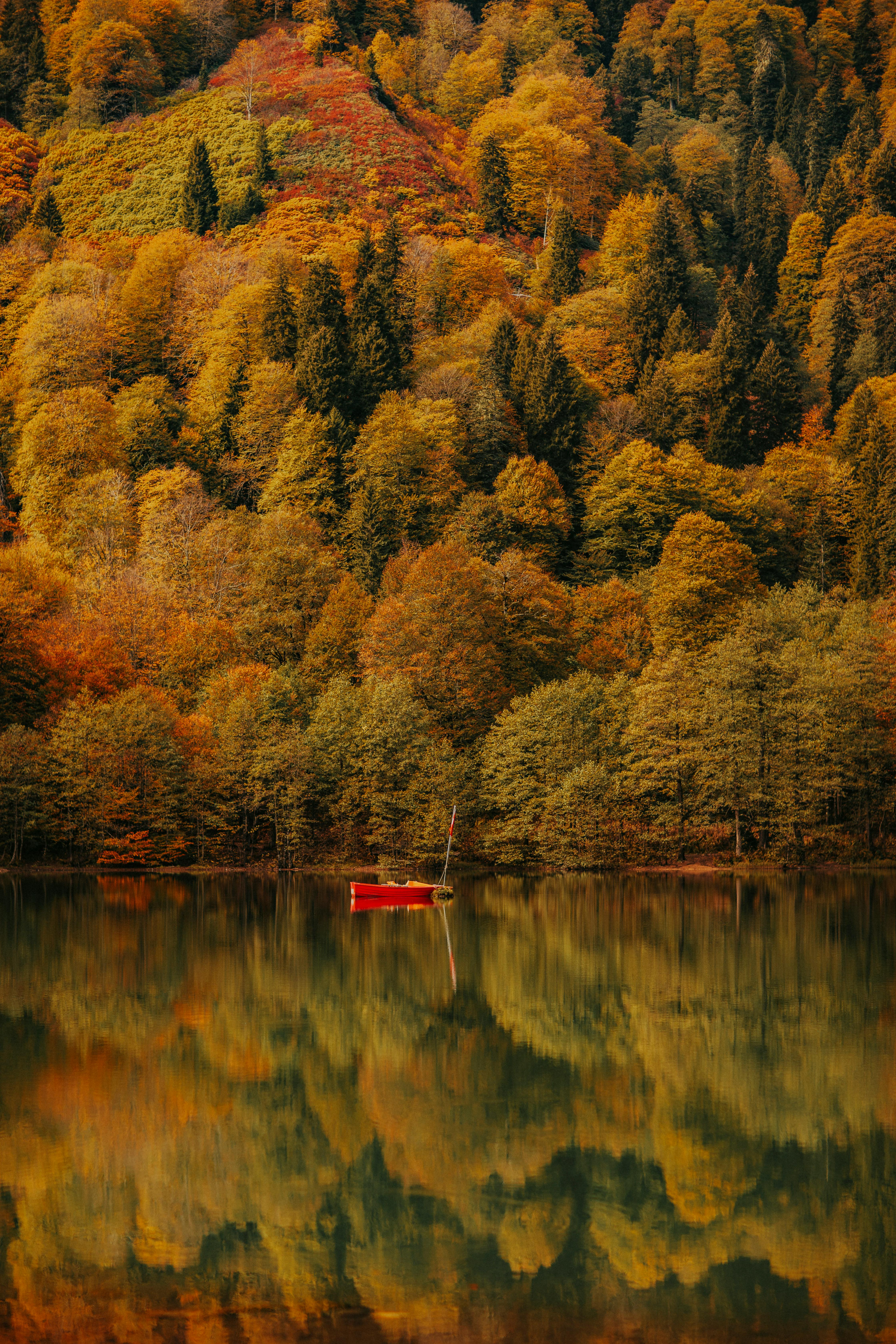 A serene lake surrounded by vibrant autumn foliage with a solitary red boat reflecting on the water.