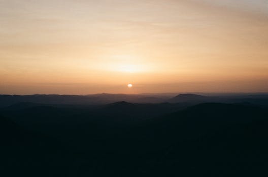 Peaceful sunrise over mountain range with silhouettes and soft colors. Perfect for nature and tranquility themes.
