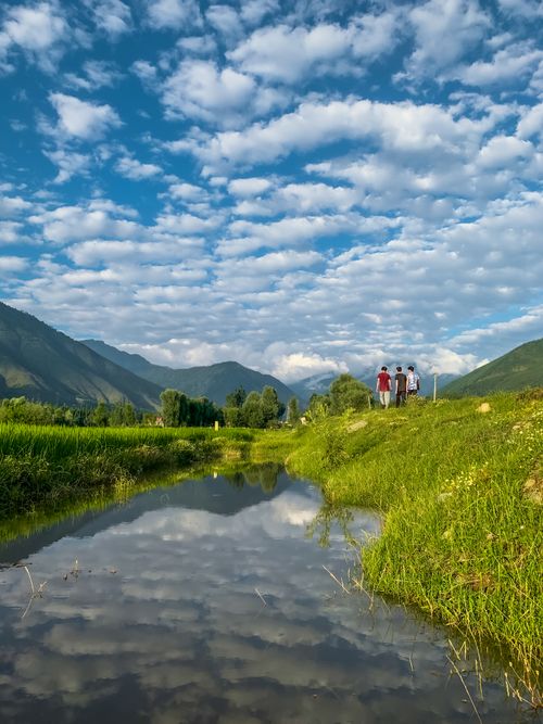 Free A serene countryside view of mountains, a river, and clouds reflecting in the water under a blue sky. Stock Photo