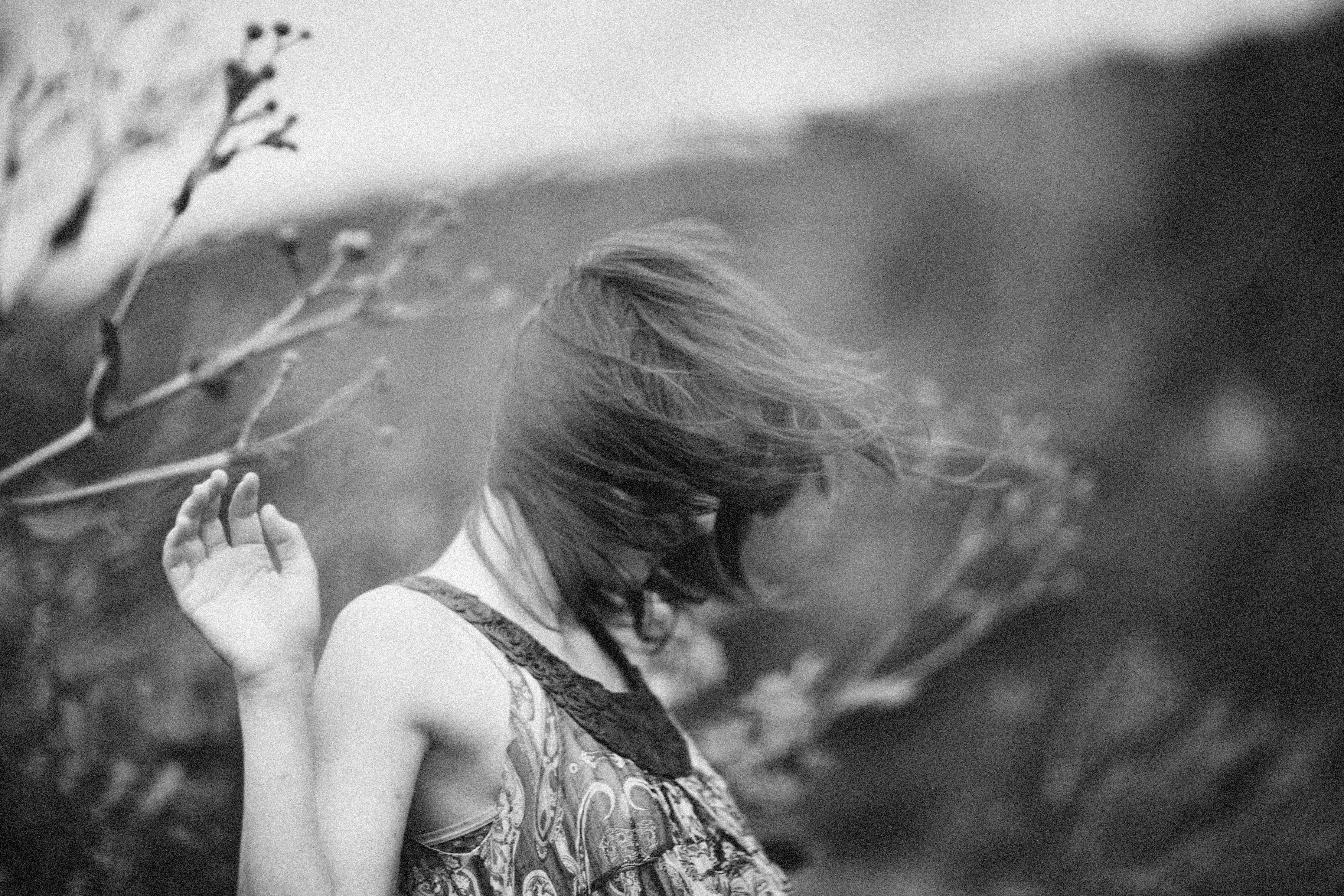 Black and white artistic portrait of a woman outdoors with flowing hair.