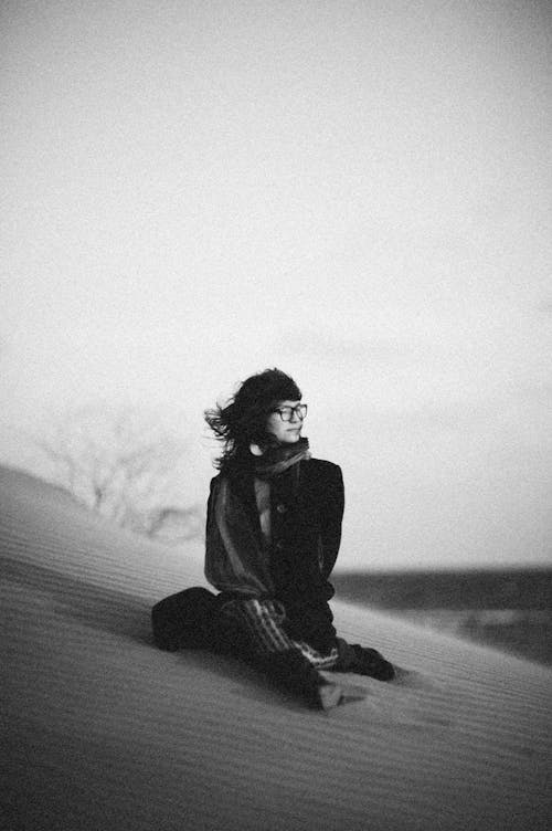 Grayscale Photo of a Woman Sitting on Sand