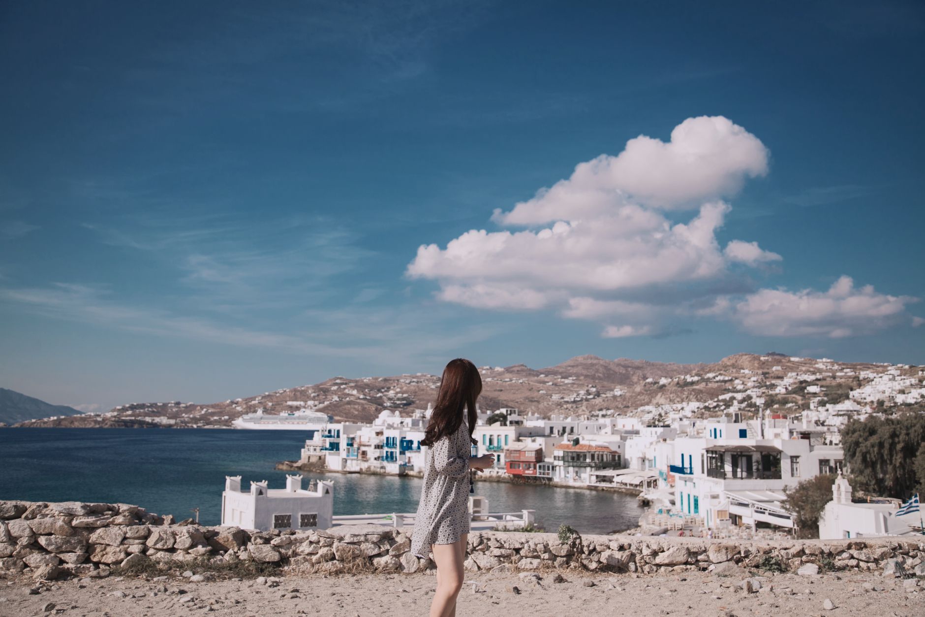 A woman enjoys the beautiful Mykonos coastline with iconic architecture under a clear blue sky.
