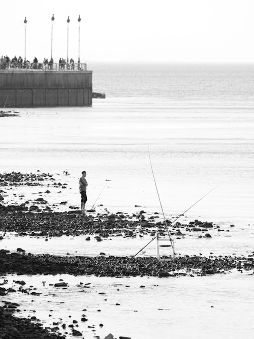 Grayscale Photo of a Man Standing on Rocky Shore