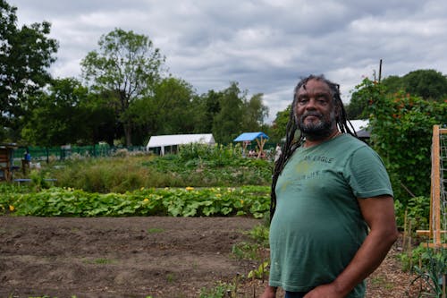 Free Positive unshaven African American male farmer with dreadlocks on head standing in garden of rural village Stock Photo
