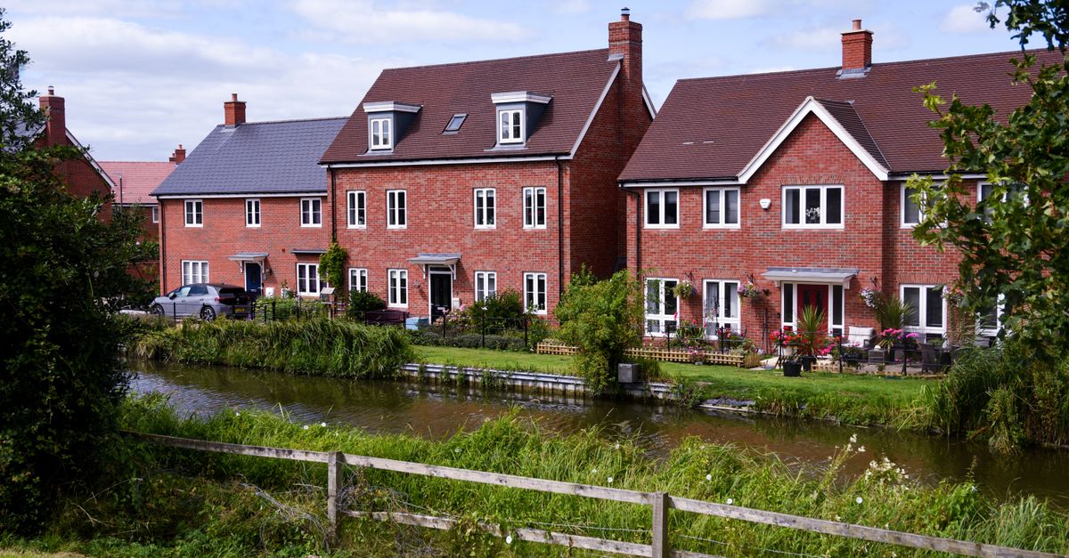 Row of brick houses with gardens by a tranquil river. Perfect urban retreat.
