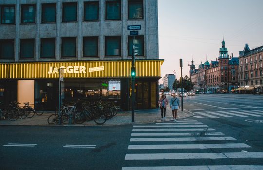 Two women walking by bicycles on a street in Copenhagen at dusk.