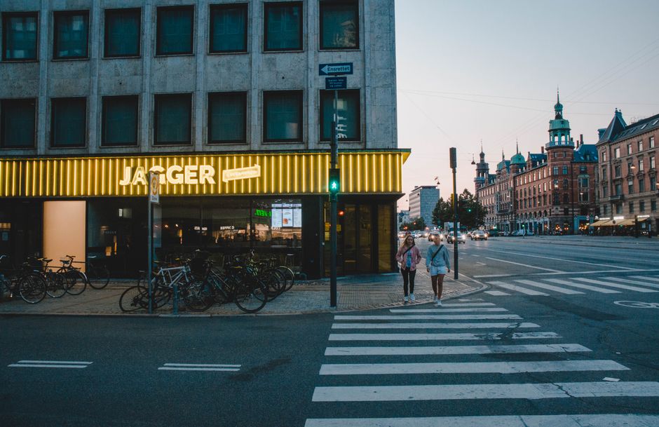 Two women walking by bicycles on a street in Copenhagen at dusk.