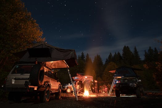 Camping scene with cars and tents under a starry night sky, featuring a cozy bonfire in the forest.