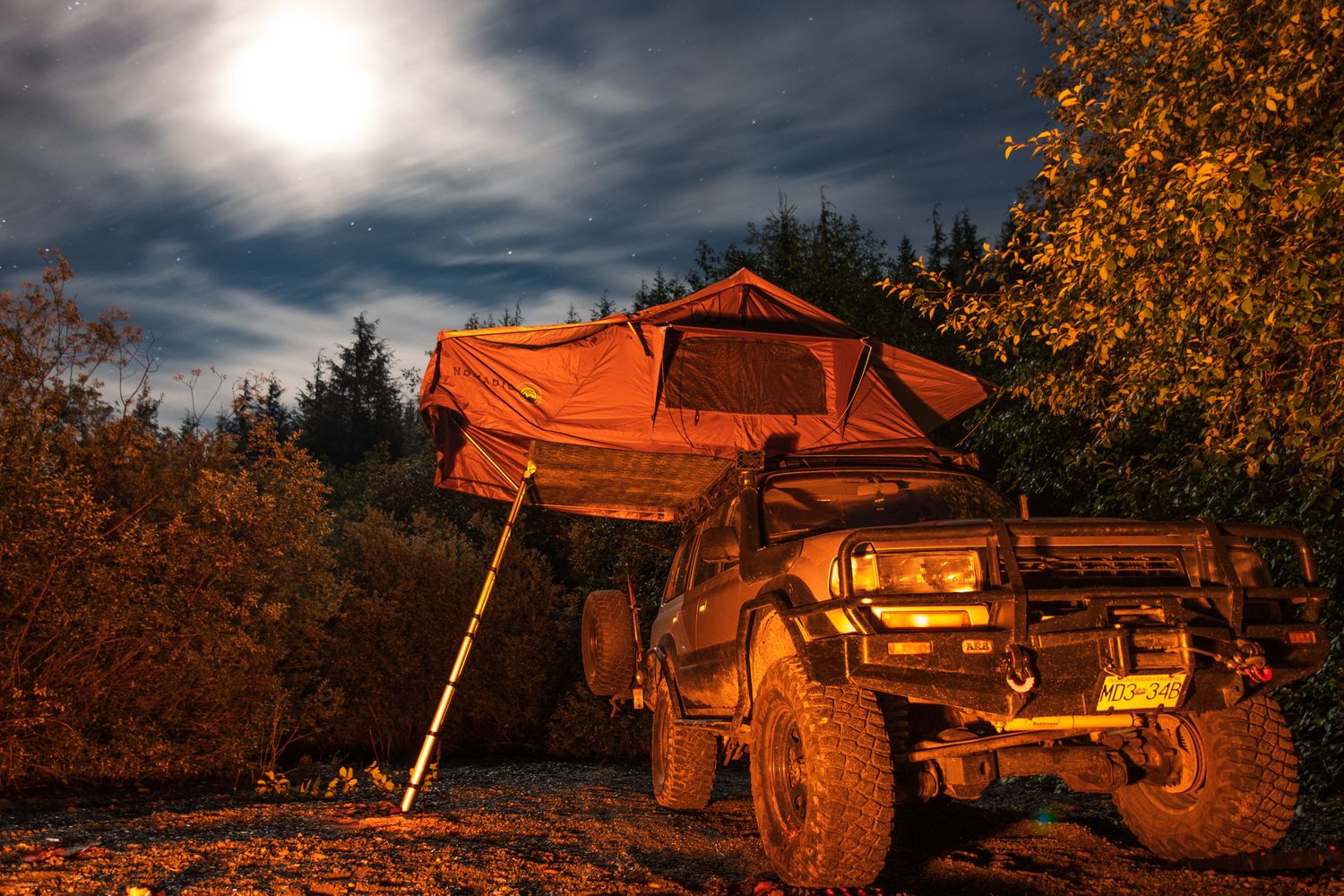 Rooftop tent with orange rainfly mounted on an off-road truck at a remote nighttime overlanding campsite