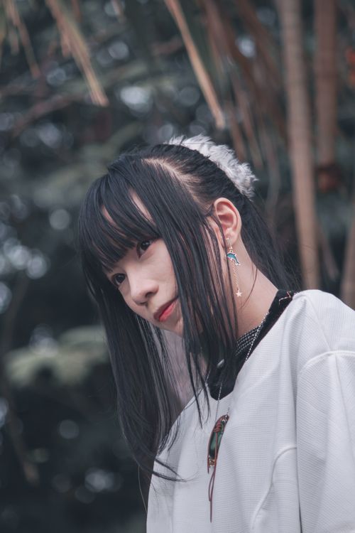 Free Stylish portrait of a young woman with straight black hair and earrings, set against a blurred natural background. Stock Photo