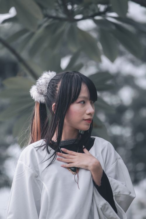 Free Portrait of an Asian woman in a stylish white dress posing outdoors with lush foliage. Stock Photo