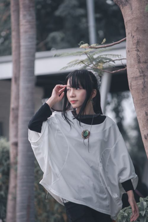 Free Young woman with black hair posing outdoors in a fashion-forward white blouse, surrounded by trees. Stock Photo