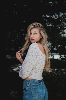 Portrait of a woman in a floral crop top and jeans, posing outdoors with a blurred background.