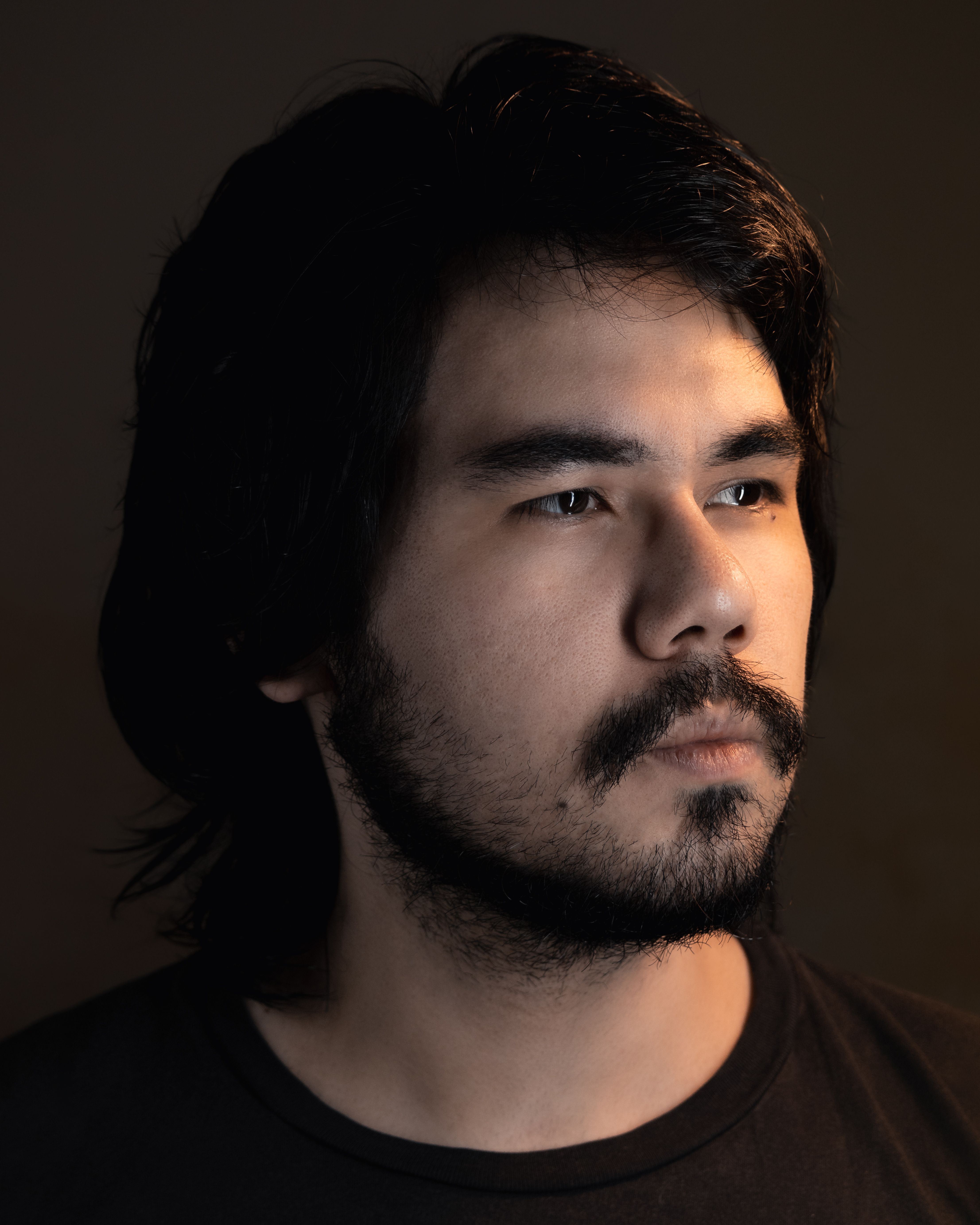 Studio portrait of an adult man with facial hair, looking serious and contemplative under soft lighting.