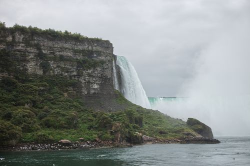 Free Majestic view of Niagara Falls waterfall cascading beside rocky cliffs on a cloudy day. Stock Photo